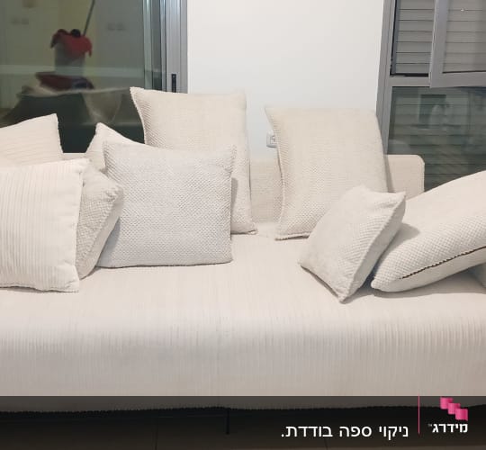ספה לבנה עם כריות רבות על רקע חלון זכוכית.